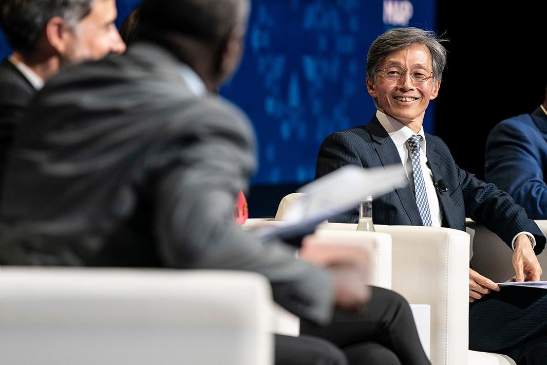 A panel discussion at an event in Morocco, featuring a man in a suit speaking while others listen attentively on stage, all seated in white chairs.