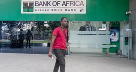 A man walking in front of a Bank of Africa branch in Ghana, wearing a red shirt and holding papers.