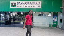 A man walking in front of a Bank of Africa branch in Ghana, wearing a red shirt and holding papers.