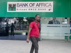 A man walking in front of a Bank of Africa branch in Ghana, wearing a red shirt and holding papers.