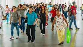 A crowded walkway in Panama filled with people walking in different directions, including women and men of various ages, some carrying bags and others looking at their phones.