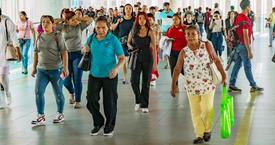 A crowded walkway in Panama filled with people walking in different directions, including women and men of various ages, some carrying bags and others looking at their phones.