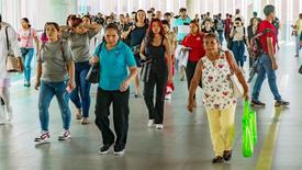 A crowded walkway in Panama filled with people walking in different directions, including women and men of various ages, some carrying bags and others looking at their phones.
