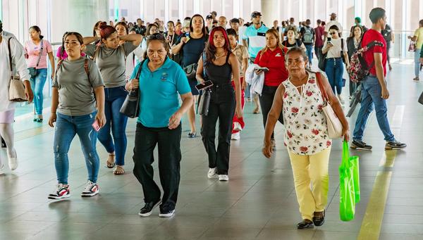 A crowded walkway in Panama filled with people walking in different directions, including women and men of various ages, some carrying bags and others looking at their phones.