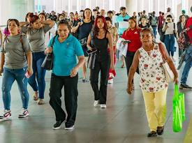 A crowded walkway in Panama filled with people walking in different directions, including women and men of various ages, some carrying bags and others looking at their phones.