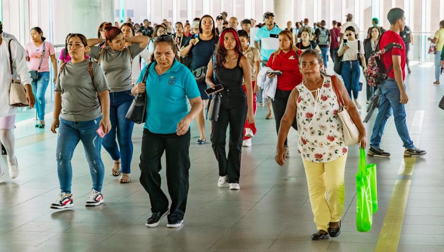 A crowded walkway in Panama filled with people walking in different directions, including women and men of various ages, some carrying bags and others looking at their phones.