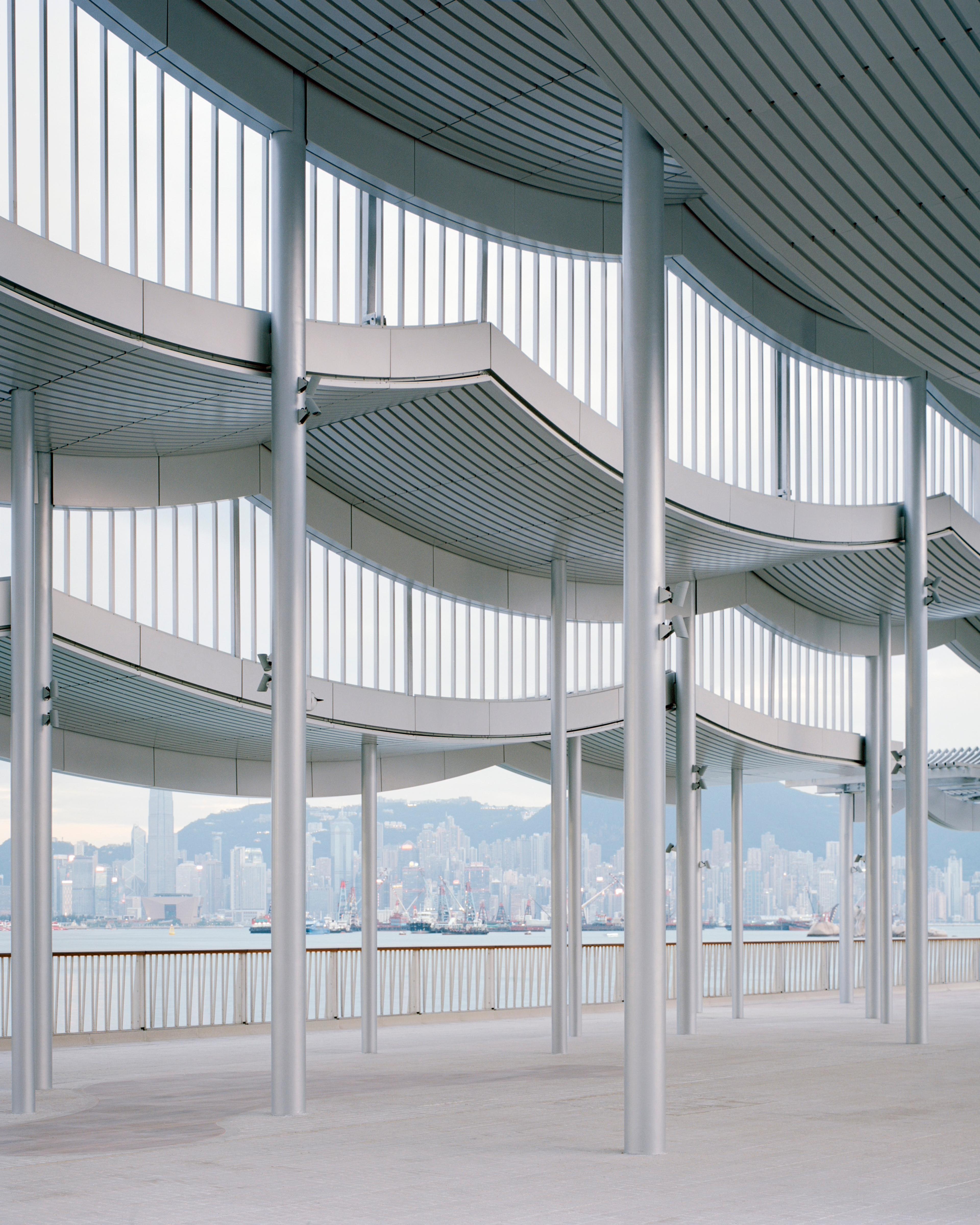 Interior of silver undulating pier canopy and Hong Kong skyline in background