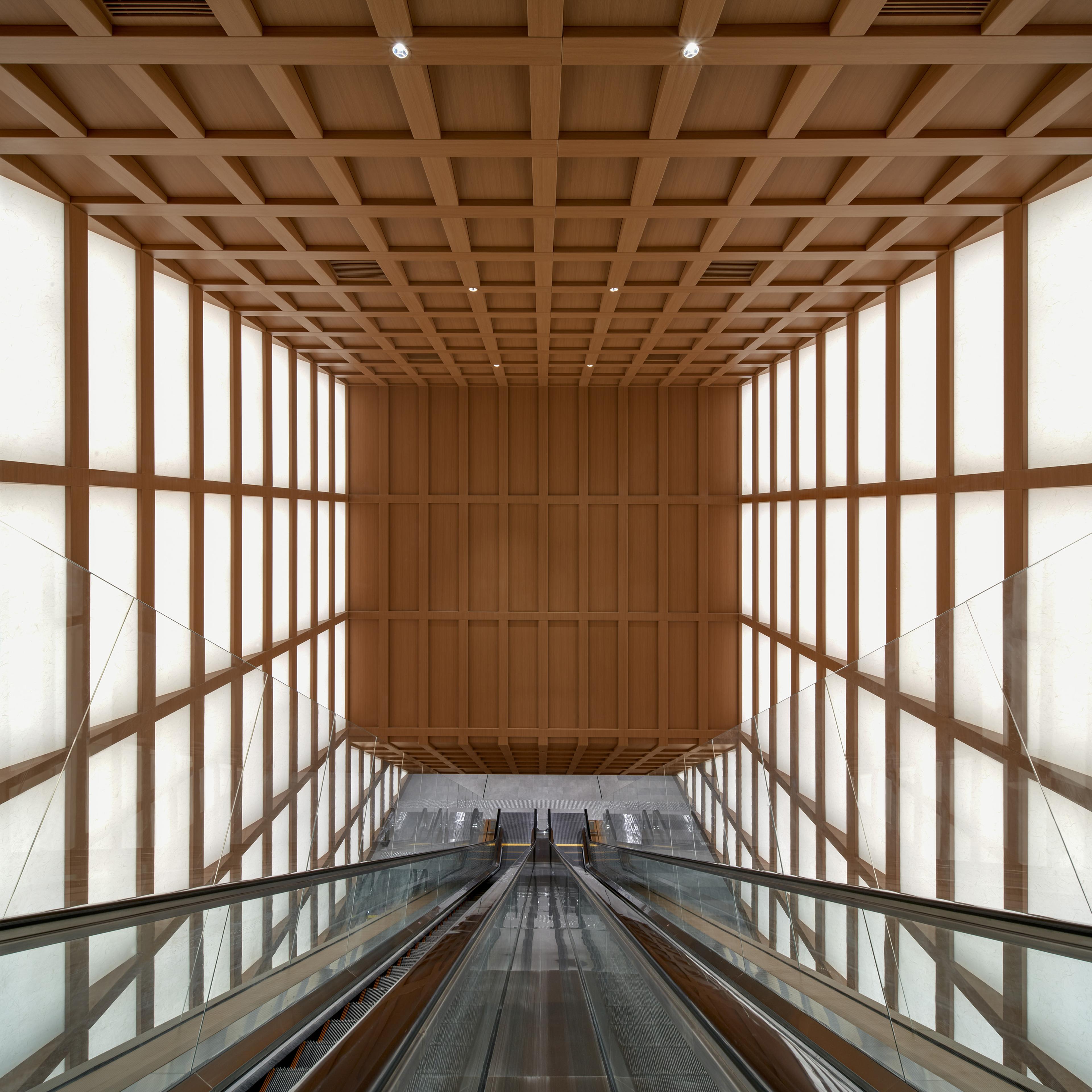 View of long escalator spanning multiple floors with timber grid ceiling and shoji light panel