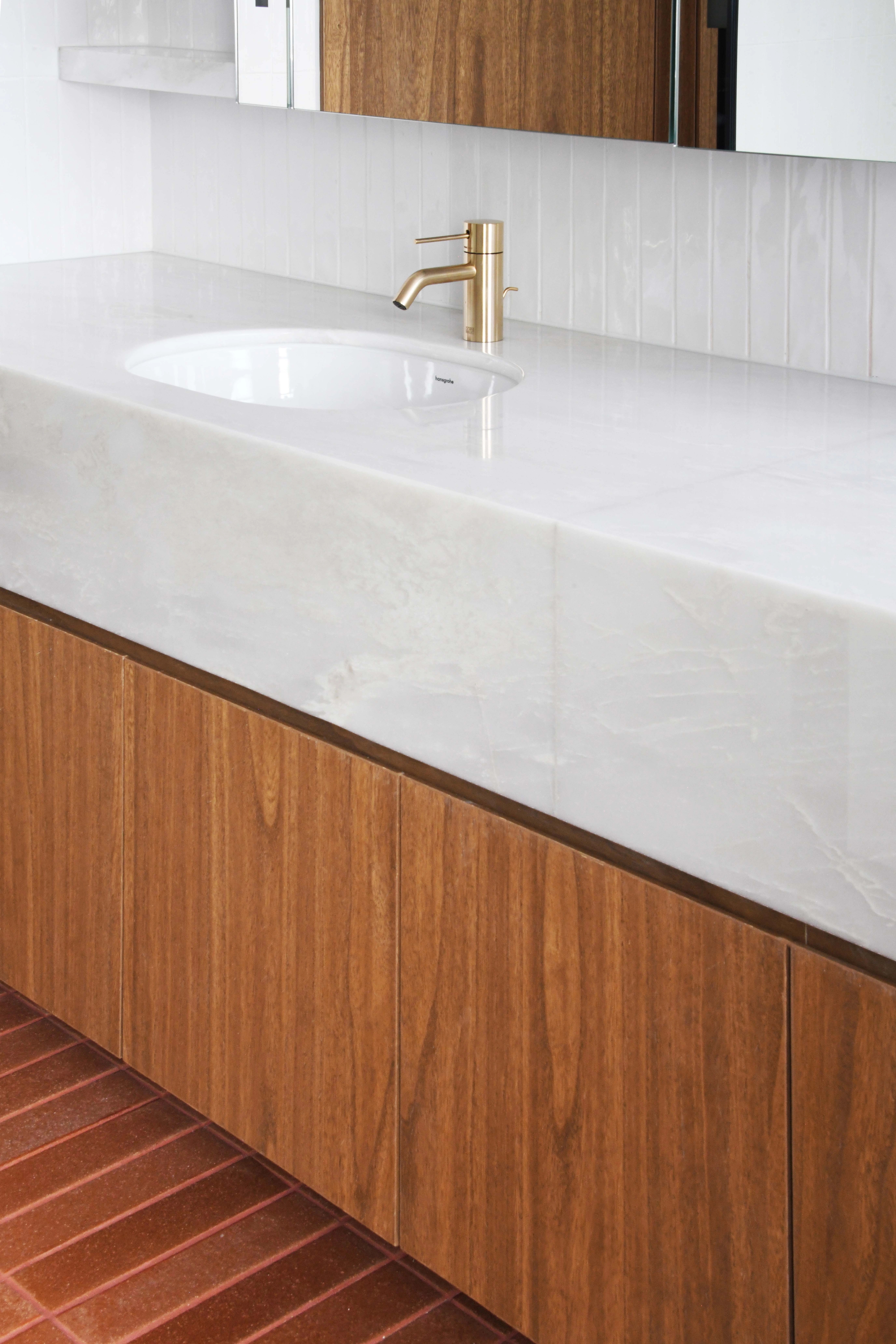 Detail of white marble vanity counter with rose gold tap and walnut cupboards
