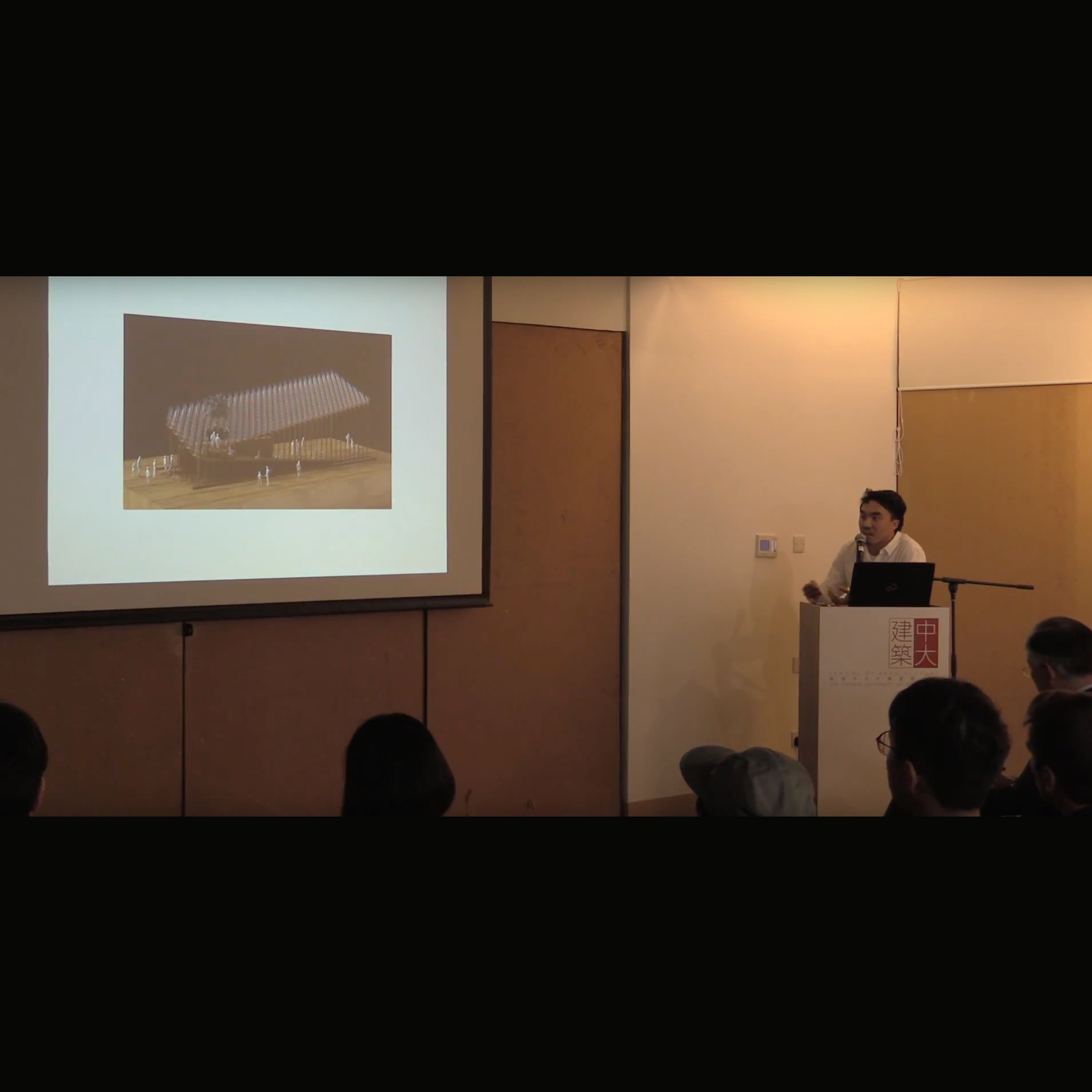 Man speaking on lectern presenting in front of screen