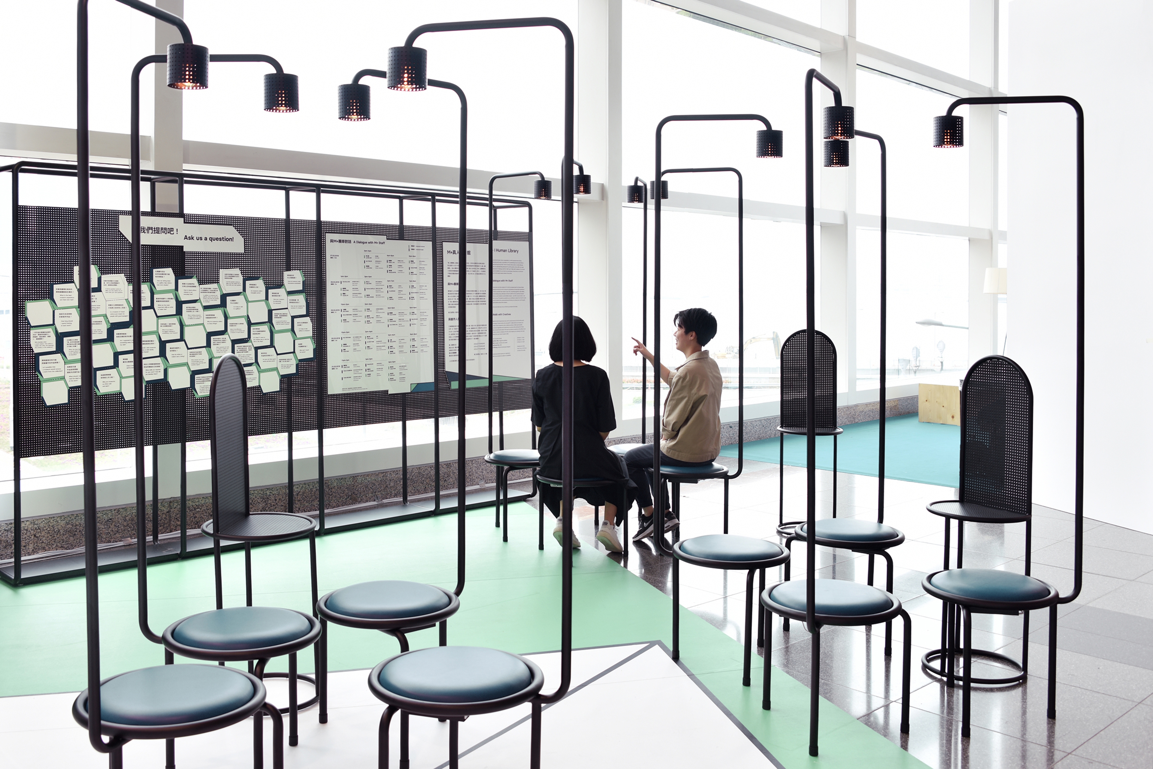 Photograph of two people sitting in art installation stools and chair and lights