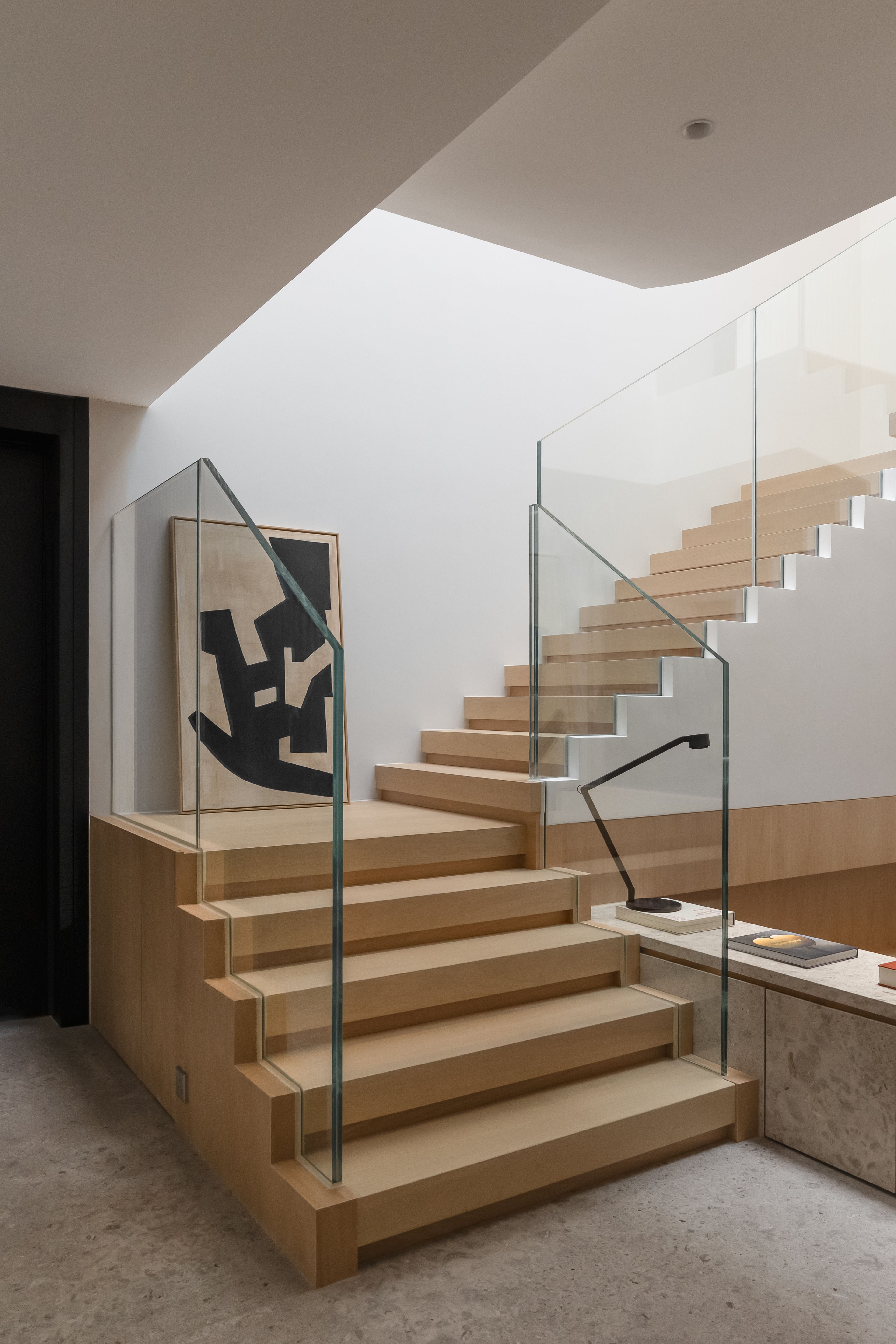 Wood stair with glass balustrade and light filtering down from skylight above