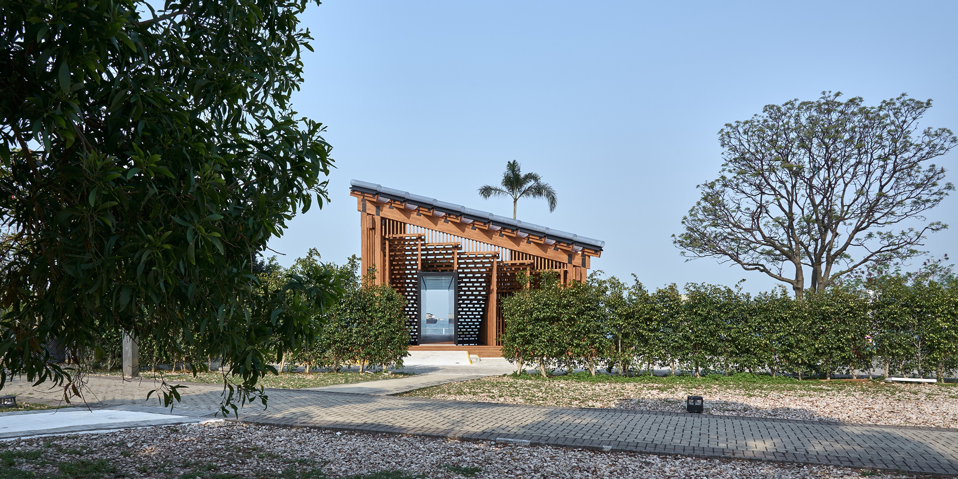 Pavilion structure in daylight with sky in background and trees and walkway in foreground