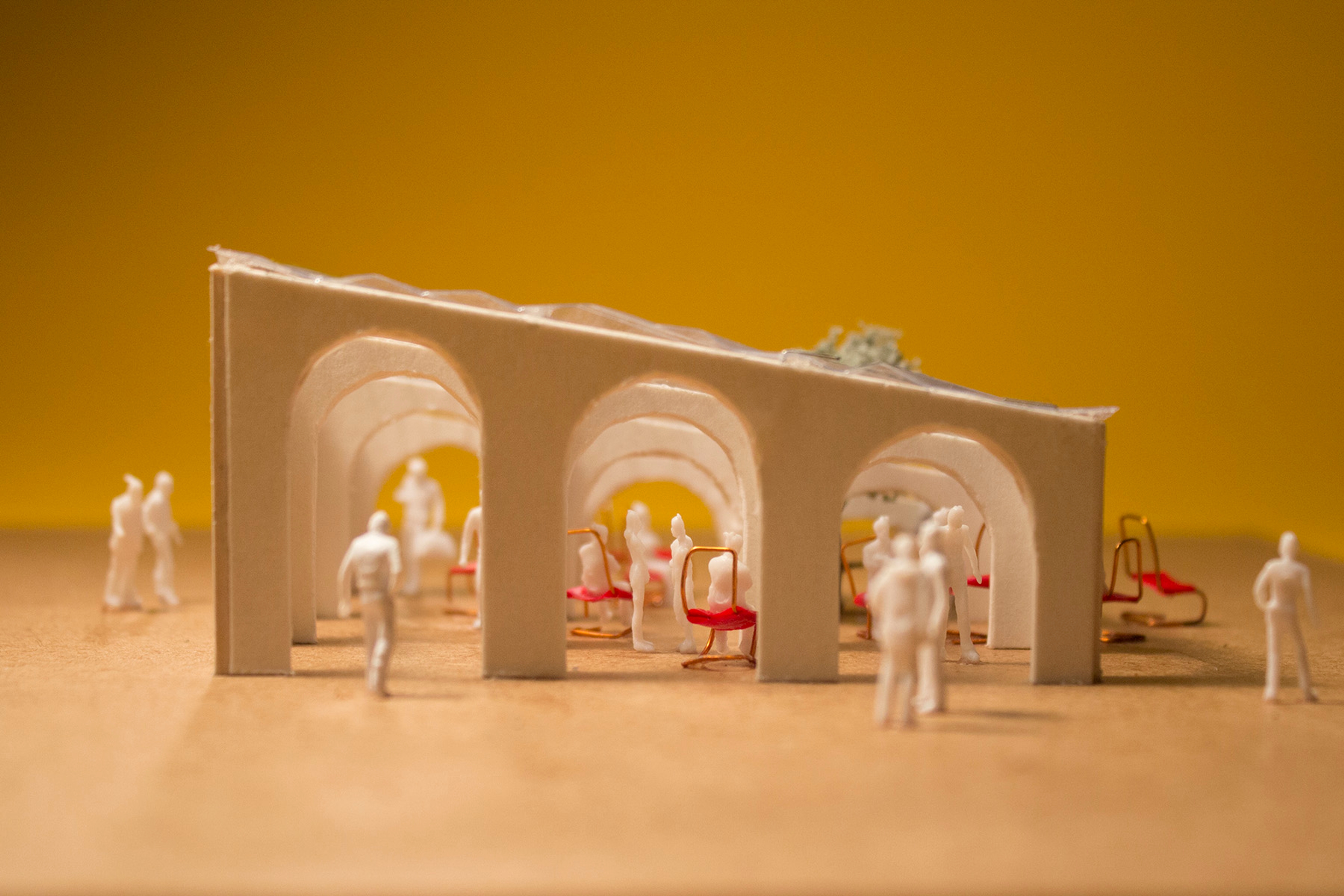 Architectural model of pavilion with chairs and people with a yellow background profile view