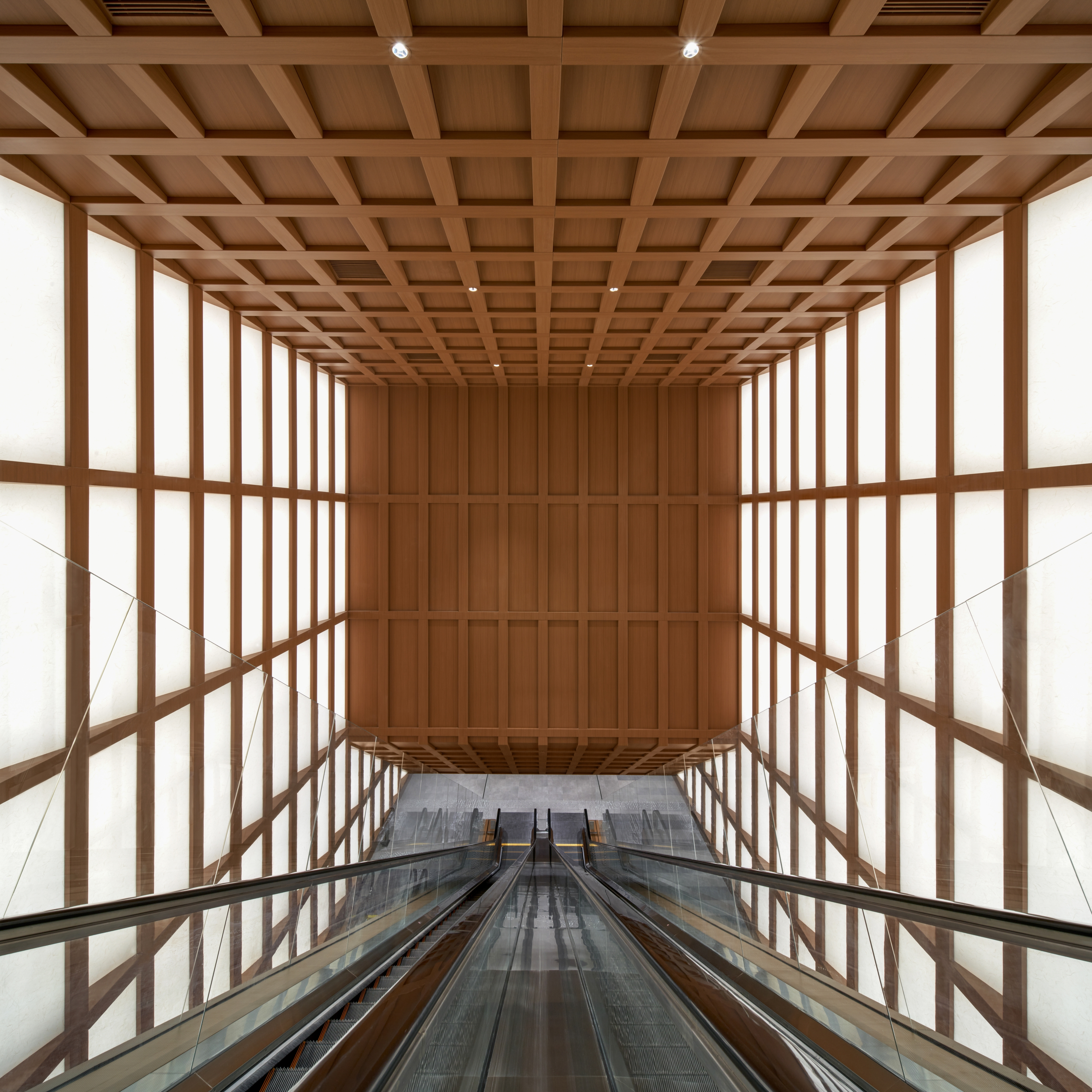 View of long escalator spanning multiple floors with timber grid ceiling and shoji light panel