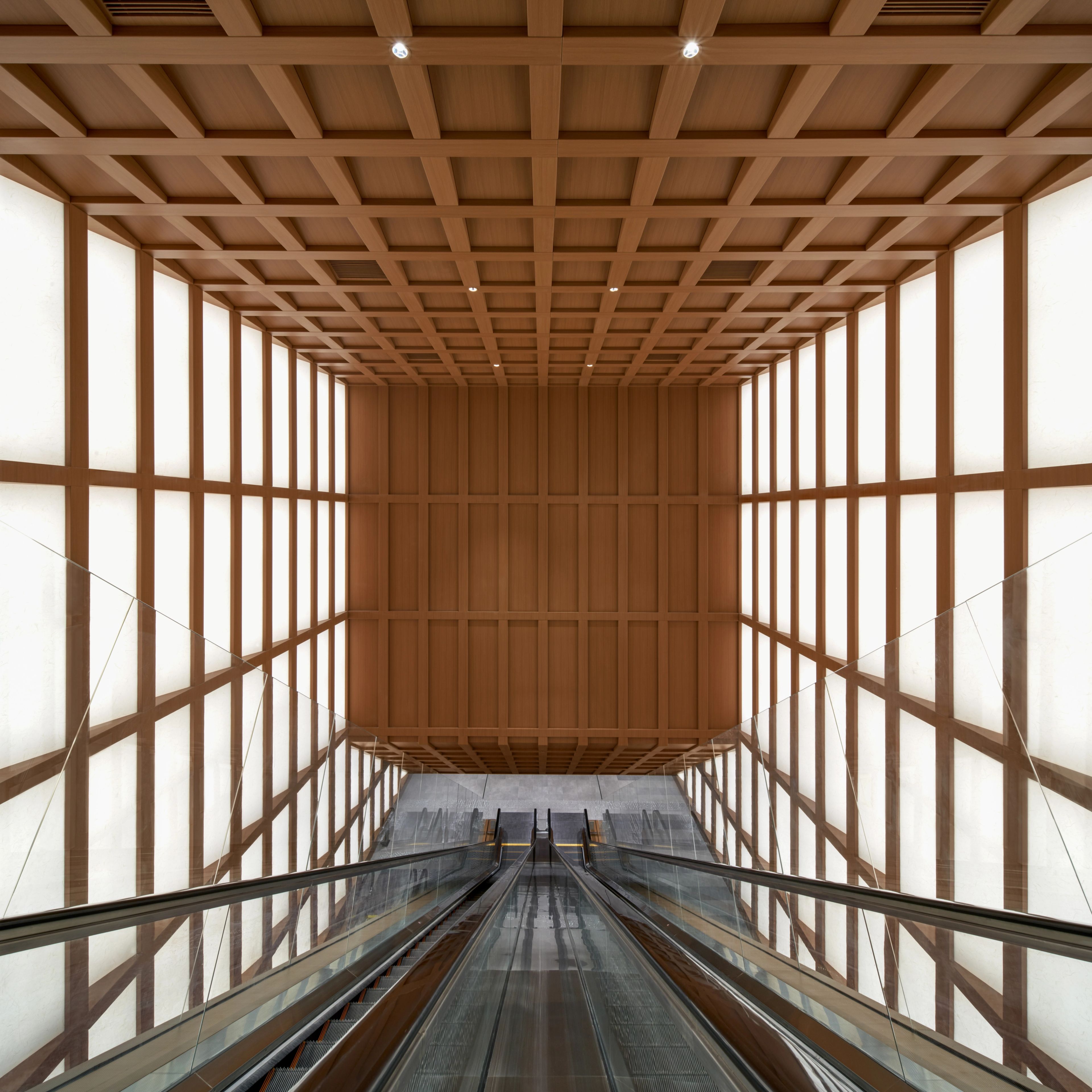 View of long escalator spanning multiple floors with timber grid ceiling and shoji light panel