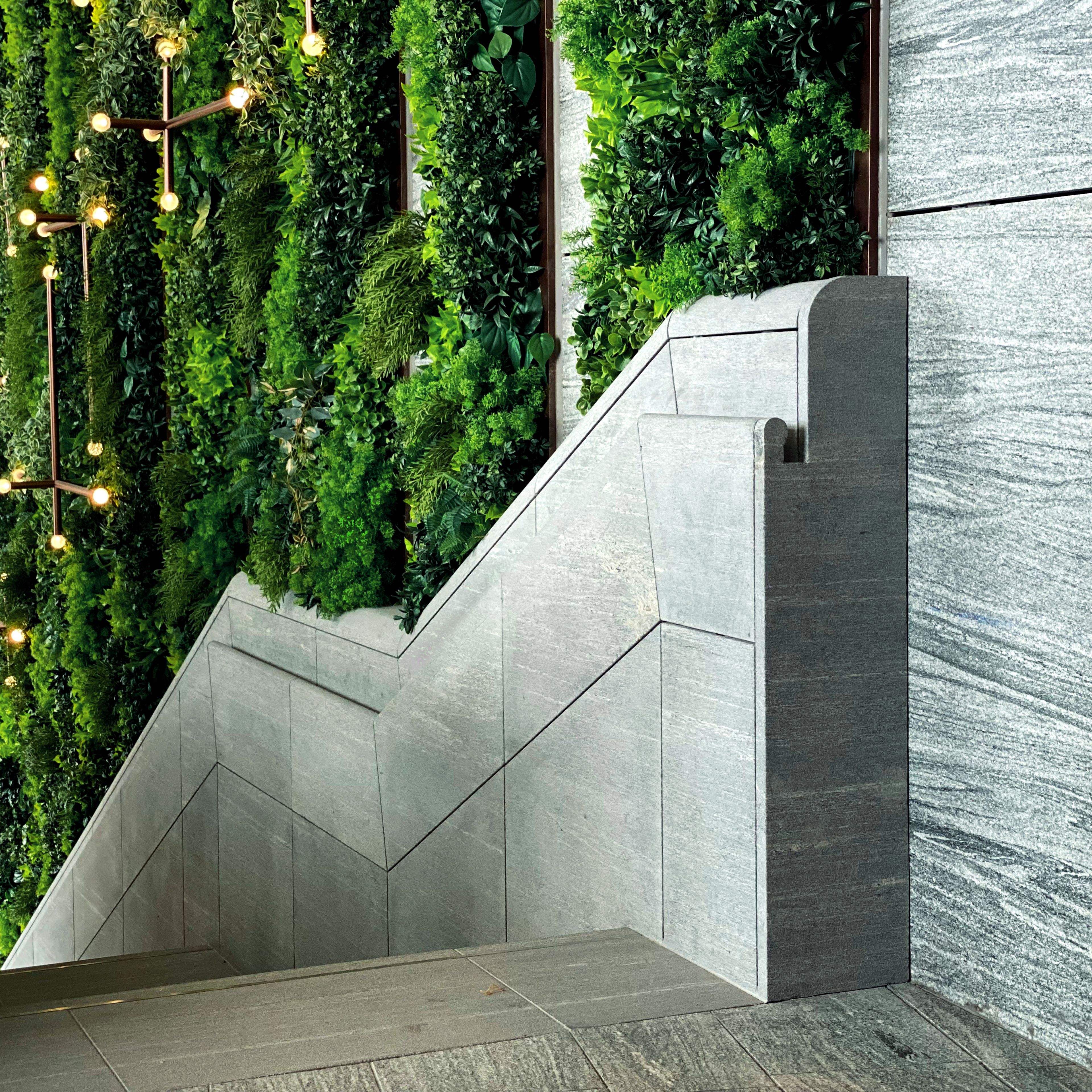 Curved grey stone balustrade with lush green wall and feature light behind