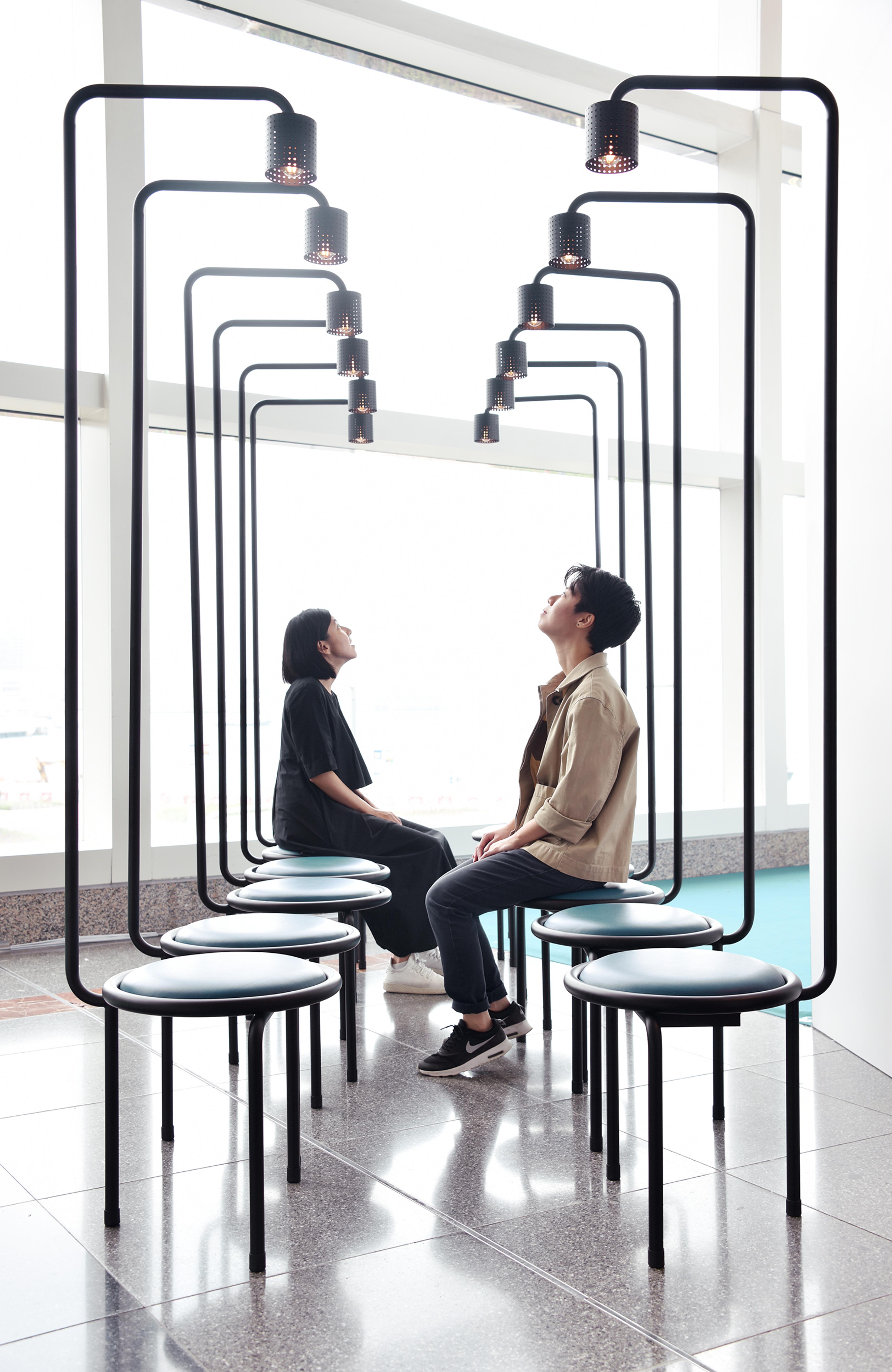 Photograph of two people sitting in art installation of stools with lights