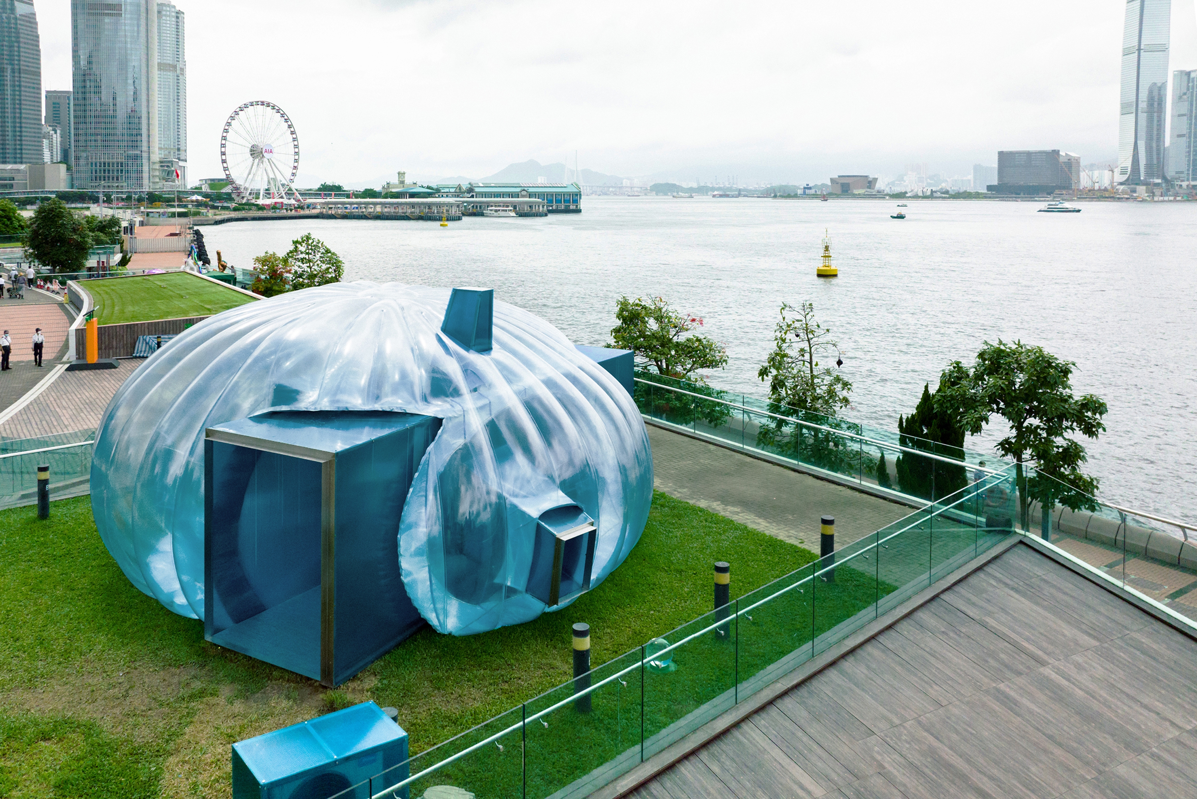 Temporary bubble art installation structure on Hong Kong harbour front with city skyline during sunset