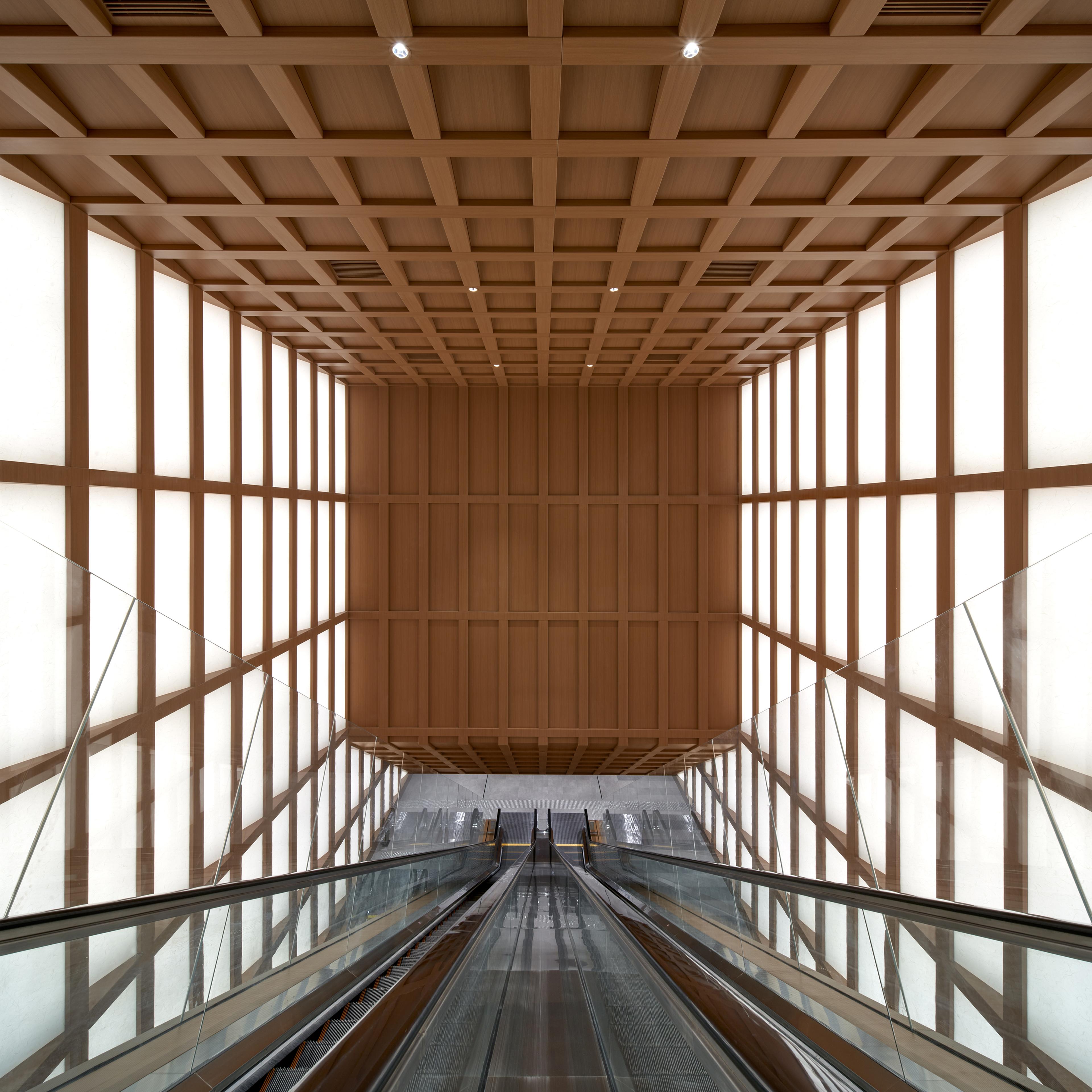 View of long escalator spanning multiple floors with timber grid ceiling and shoji light panel