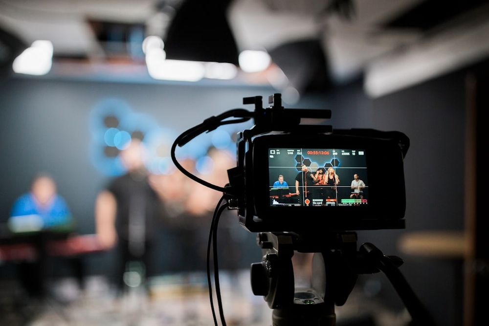 A small team of 3 people preparing for a livestream session - one adjusting lights, one checking phone comments, one arranging products on a table