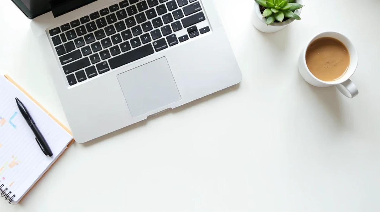 Clean desk flat-lay with laptop, notebook, and coffee