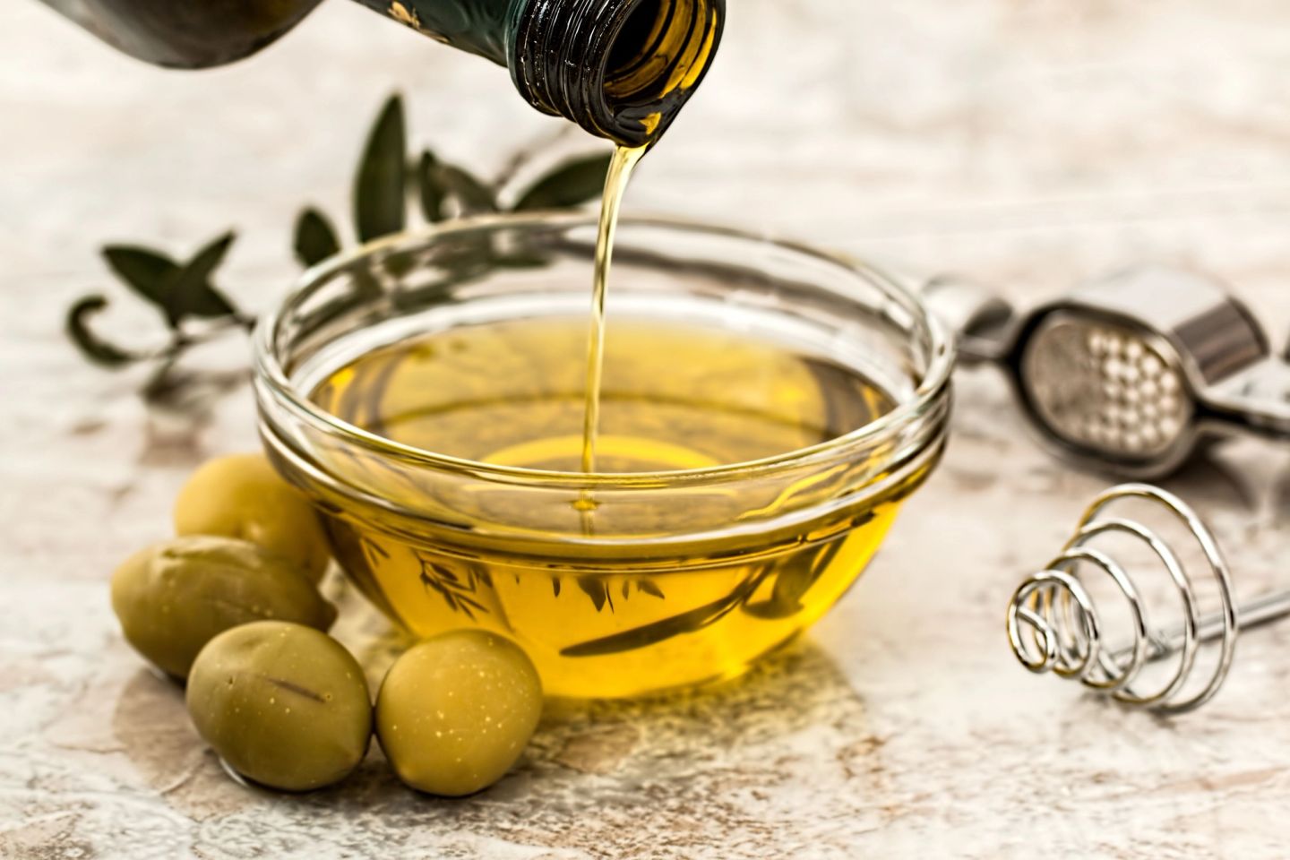 Olive oil poured into a glass bowl beside green olives