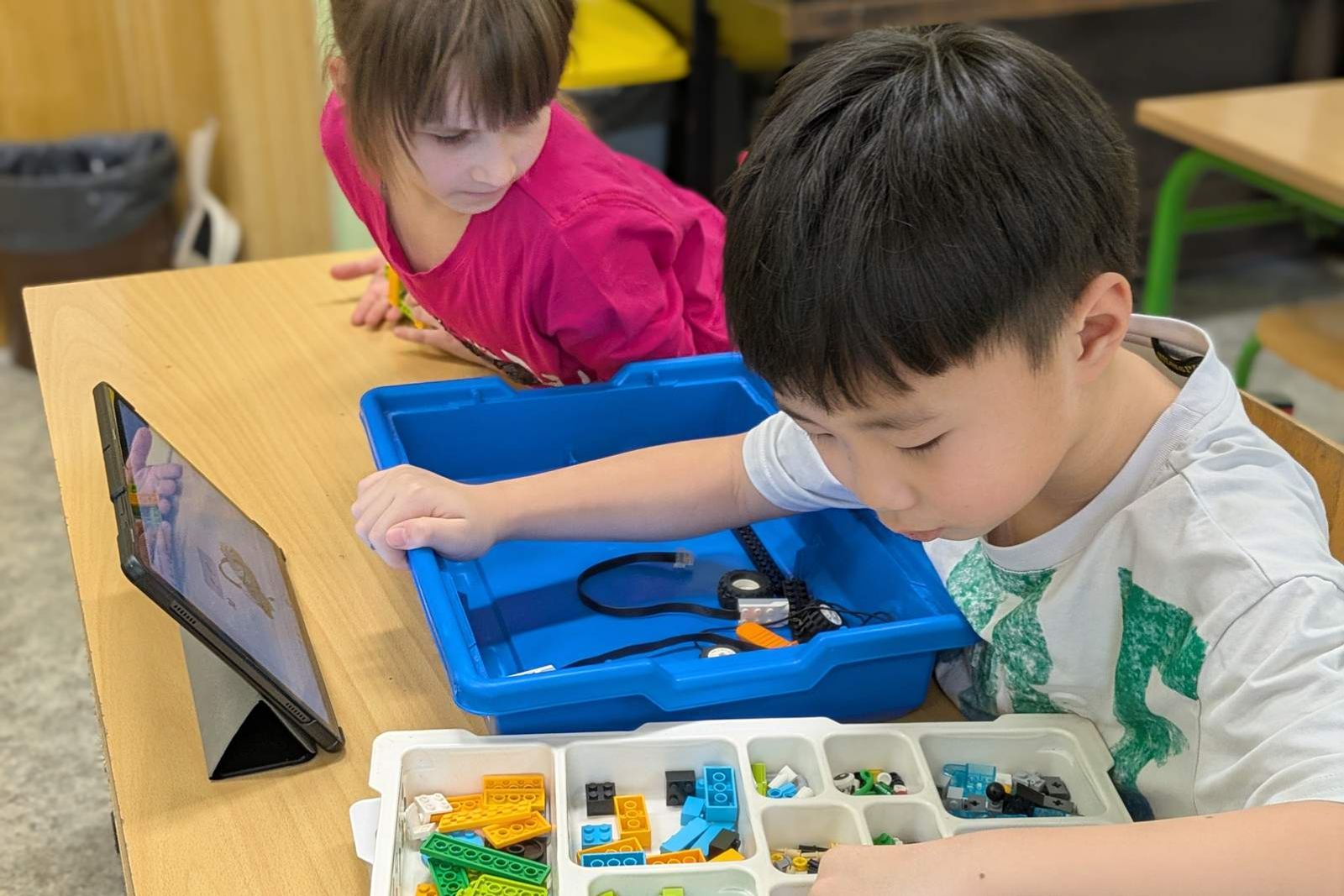 Dvojice dětí staví LEGO robota podle digitálního návodu na tabletu