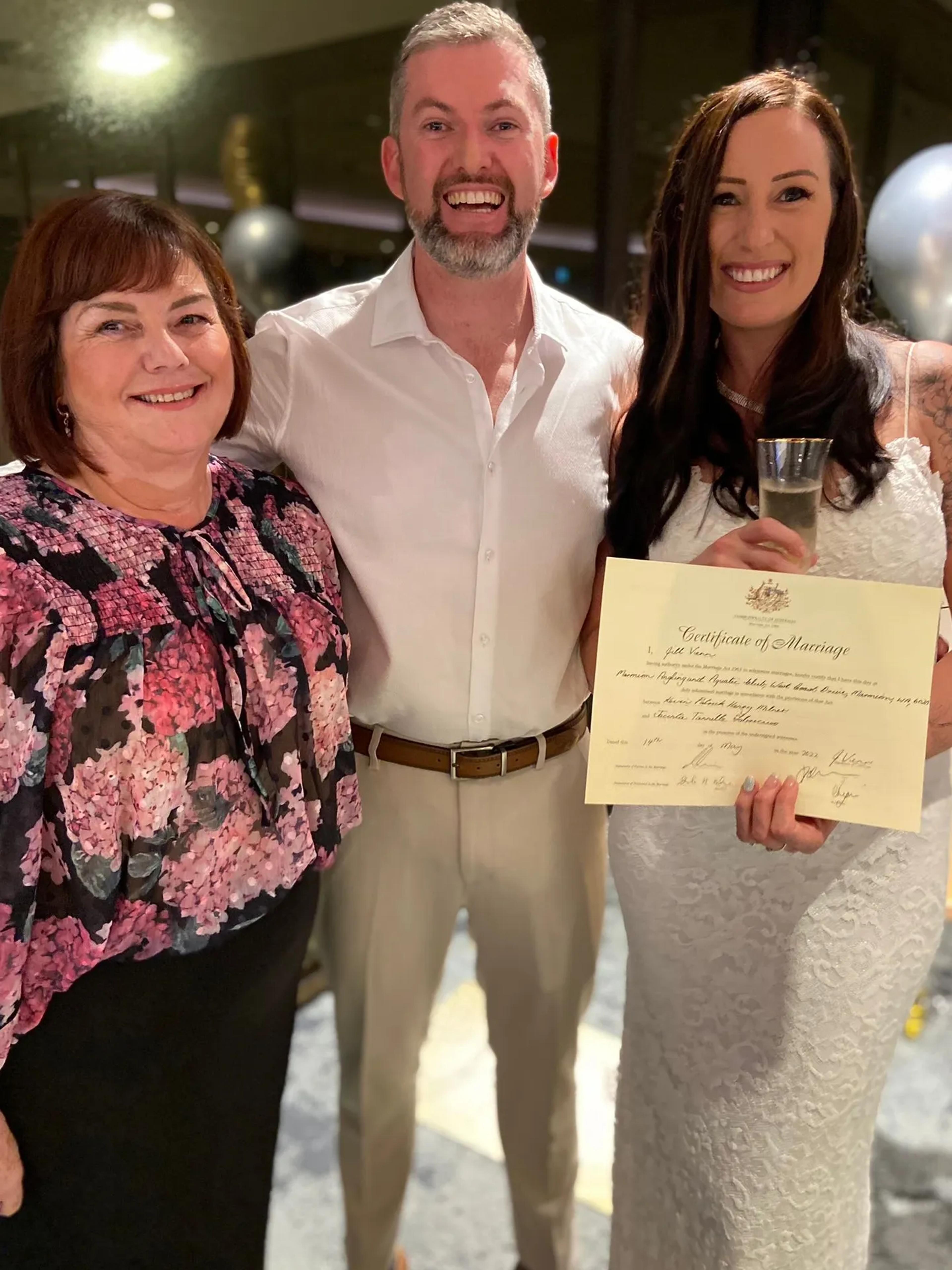 A photo of a man and a woman standing wth their wedding celebrant, holding their celebratory wedding certificate.