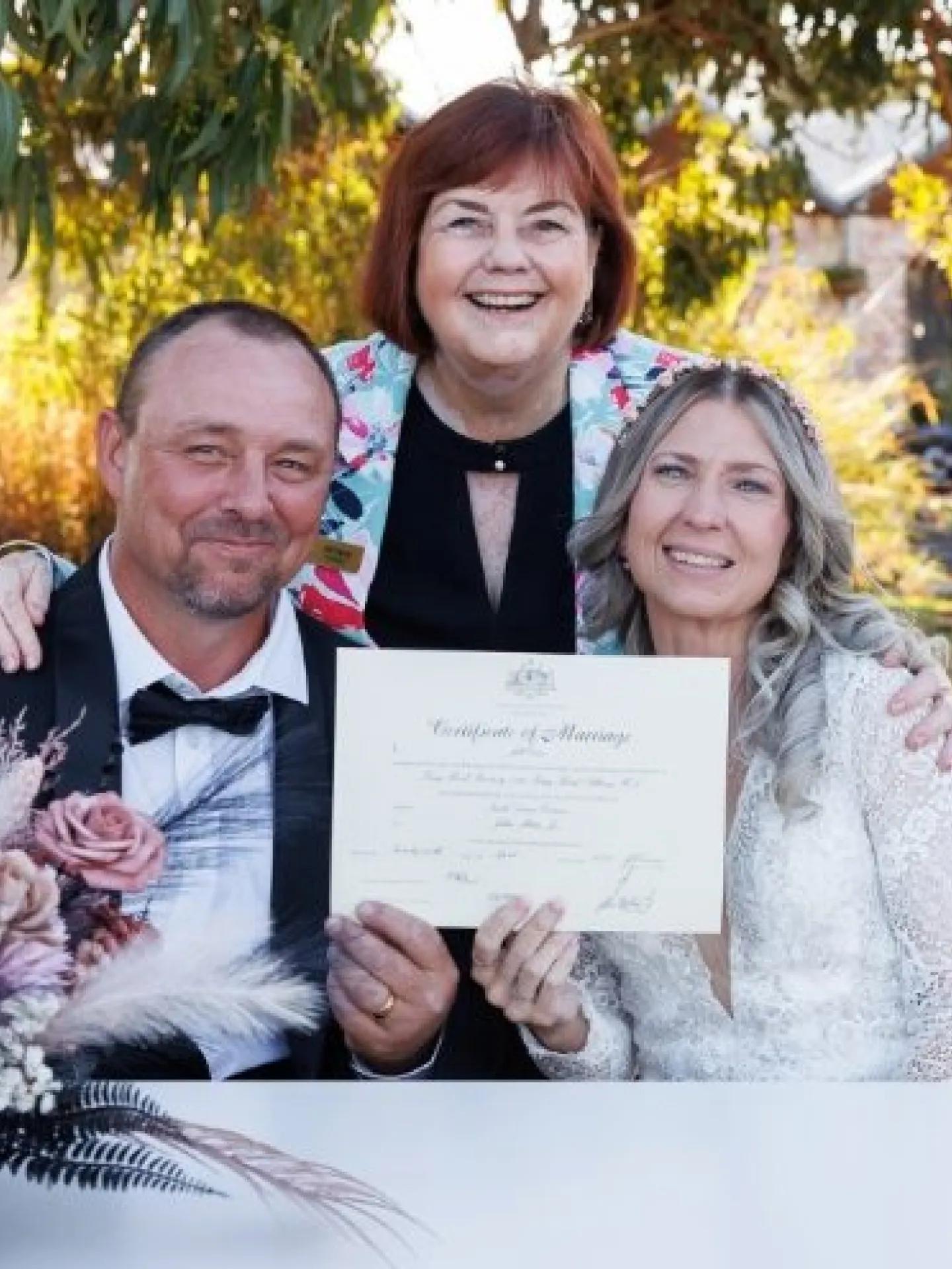 A photo of a couple sitting, holding a wedding certificate.