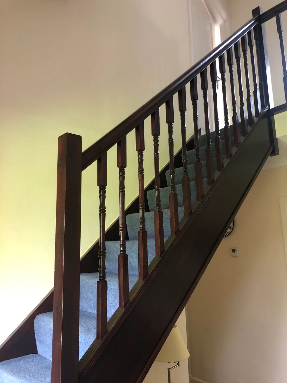 Carpeted staircase with dark wood newel post, stringers, and turned spindles supporting a matching handrail.
