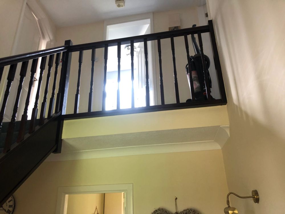 Staircase and mezzanine balcony with dark wood spindles and handrail, looking up toward a brightly lit doorway.