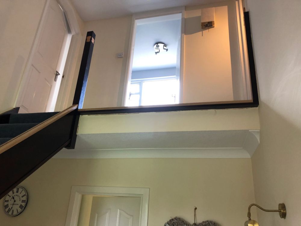 View looking up from a hallway at a first-floor landing with an open doorway, window, and ceiling light.