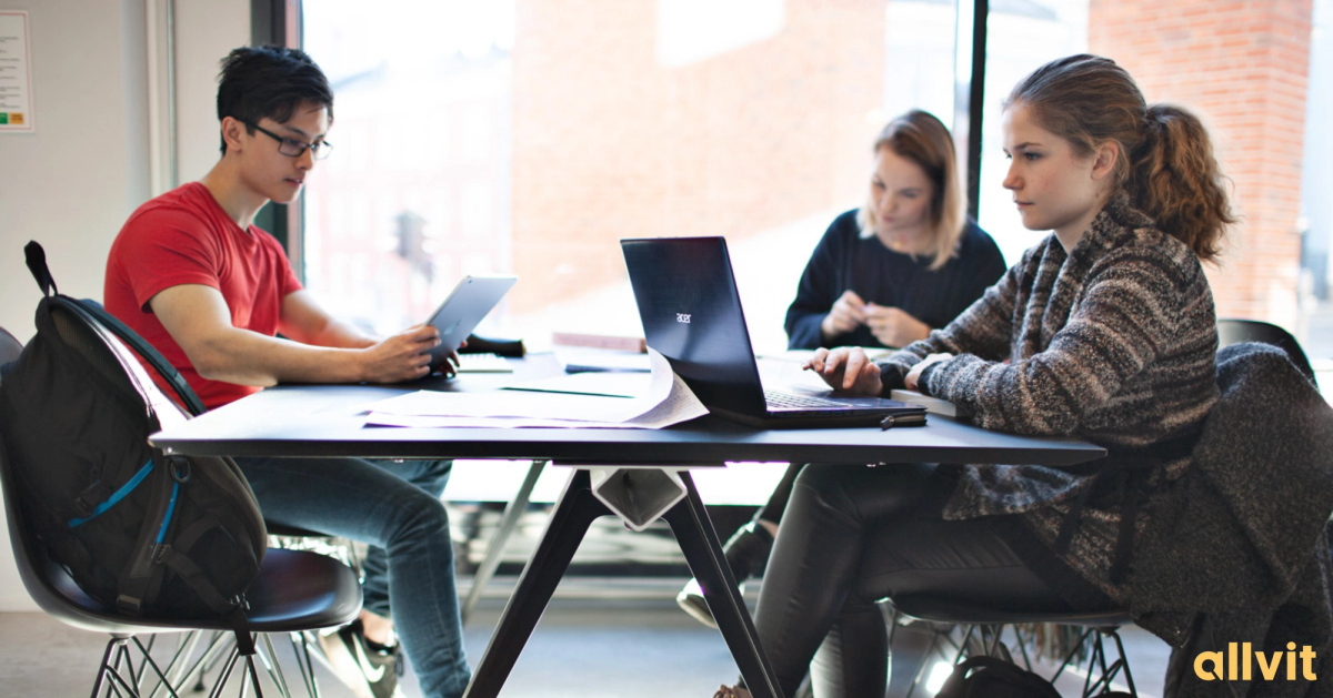 Tre studenter rundt et bord på campus. Foto.