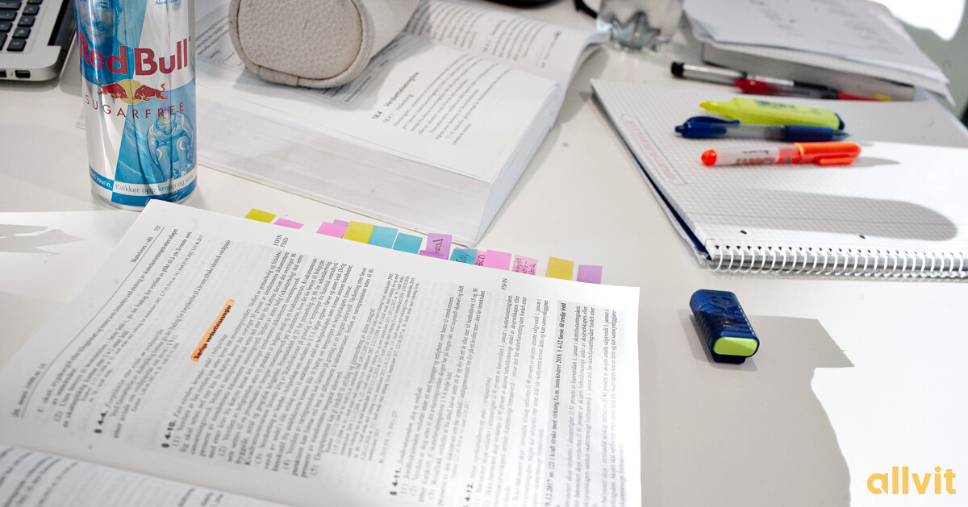 En skolepult fylt med pensumbøker, markeringstusjer, et pennal og en RedBull. Foto.