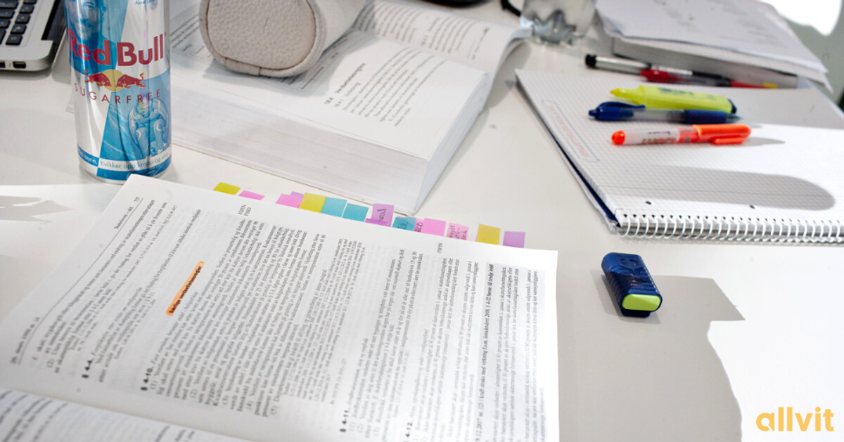 En skolepult fylt med pensumbøker, markeringstusjer, et pennal og en RedBull. Foto.