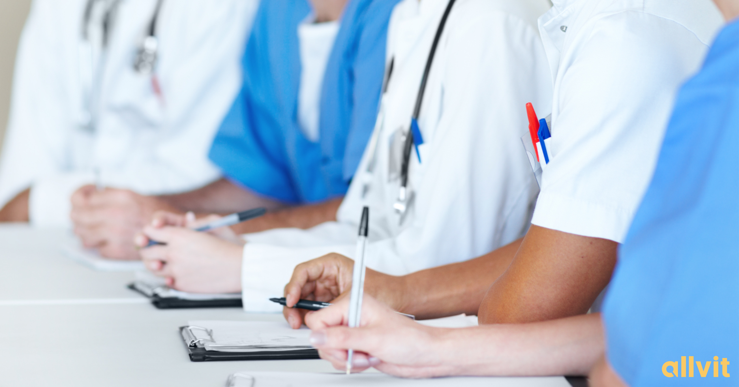 Studenter i helsefrakk med penn og papir foran seg. Foto.