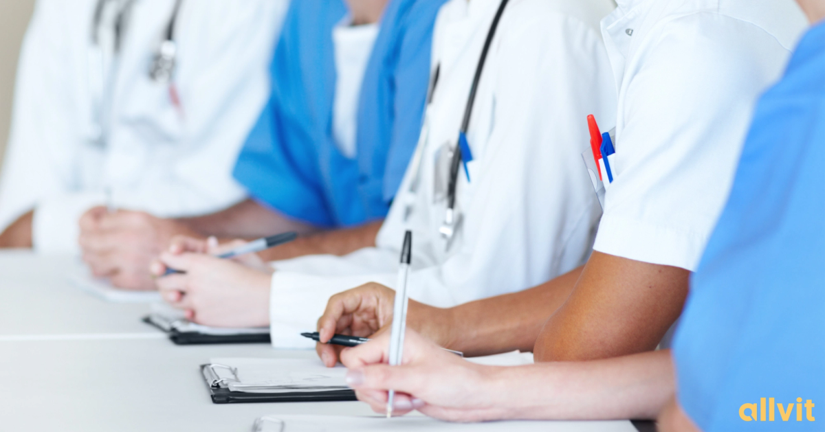 Studenter i helsefrakk med penn og papir foran seg. Foto.