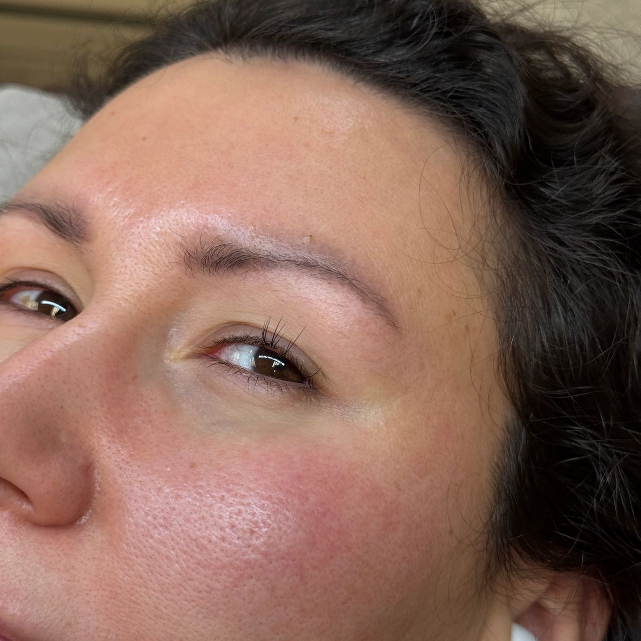 Close-up of a person's right eye with natural lashes wearing a white earbud.
