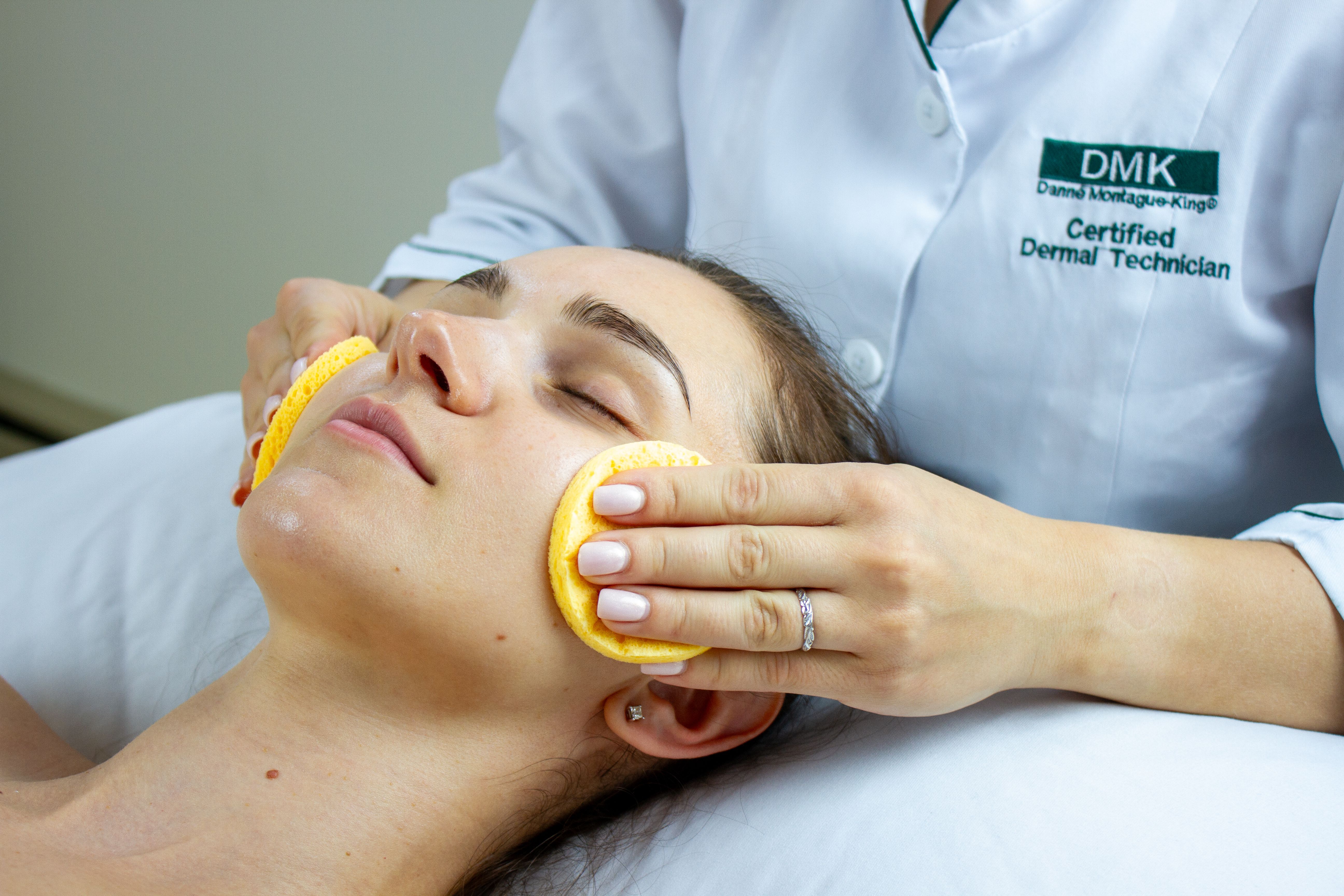 A skin specialist cleanses a woman's face with yellow sponges.
