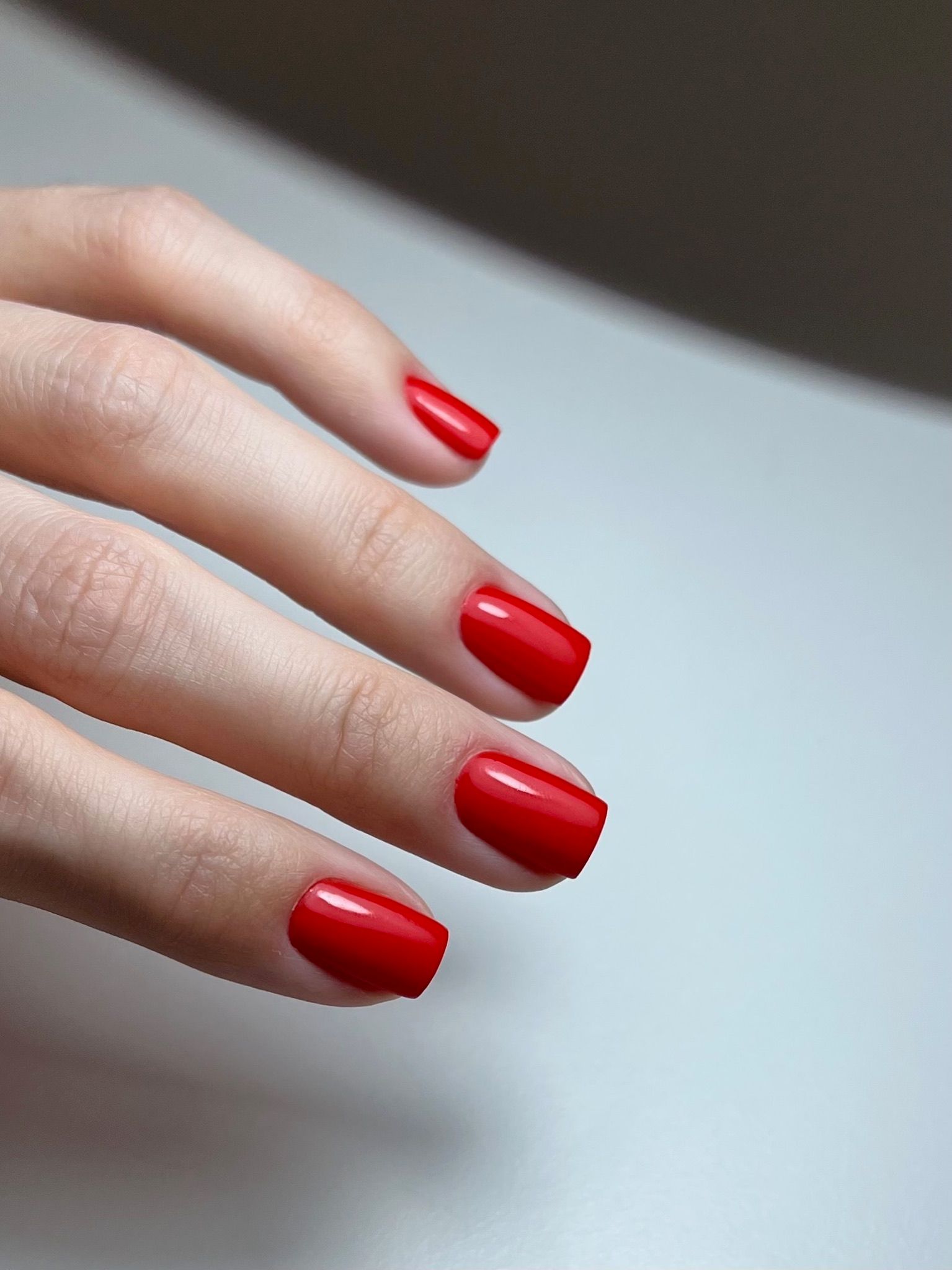 A hand with short, square-shaped nails painted bright red.