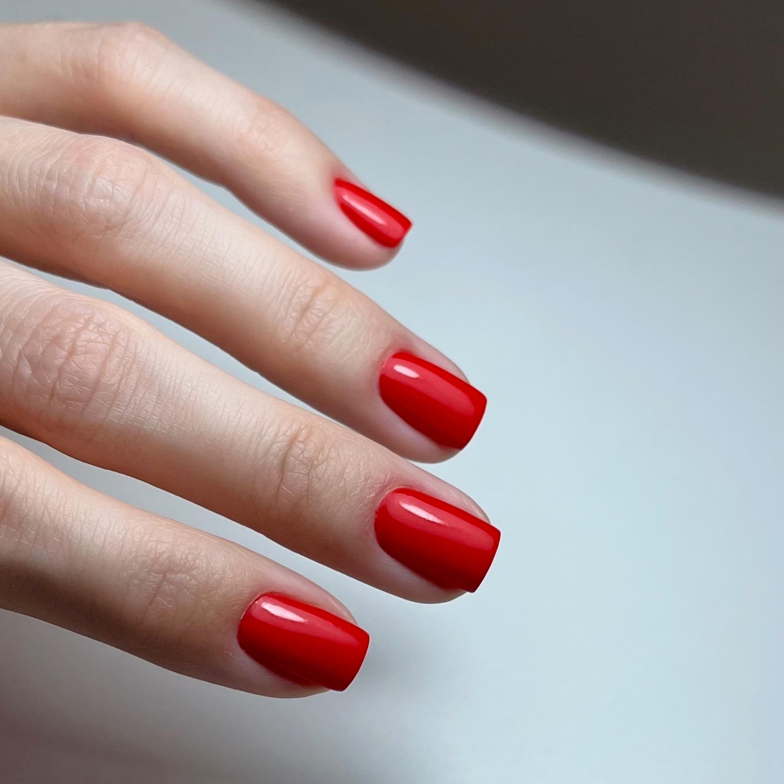 A hand with short, square-shaped nails painted bright red.