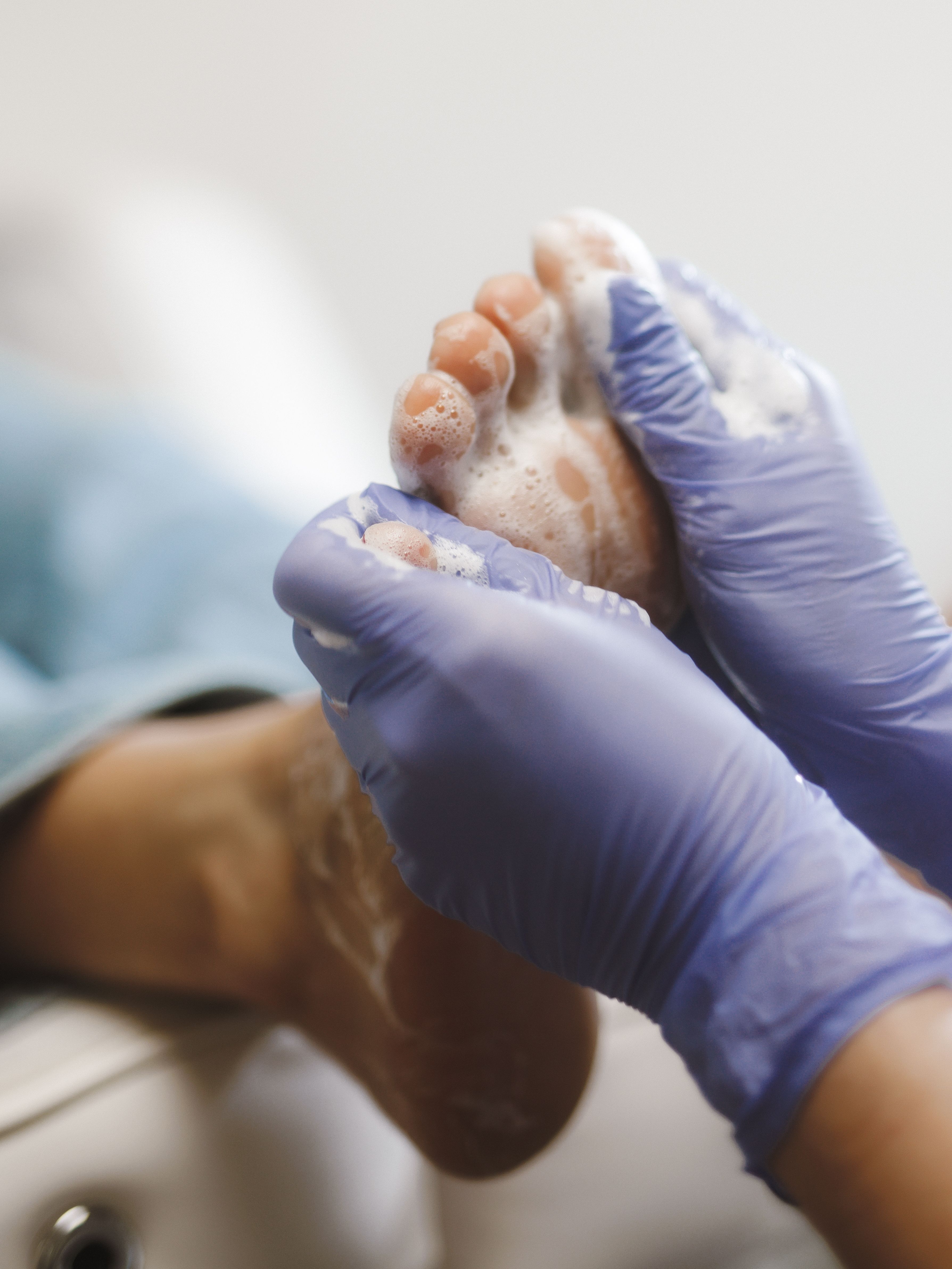 Gloved hands washing a soapy foot.