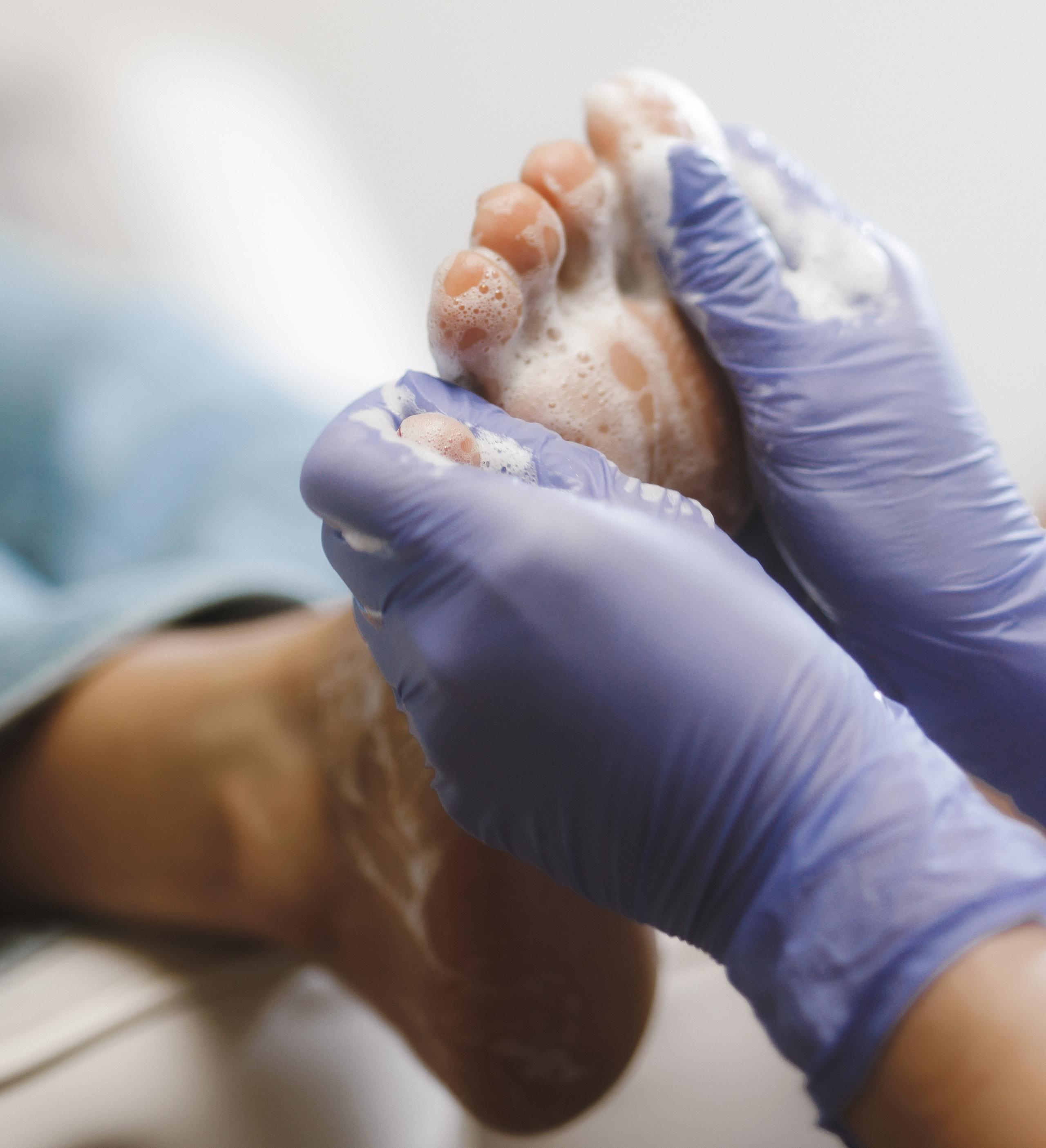 Gloved hands washing a soapy foot.