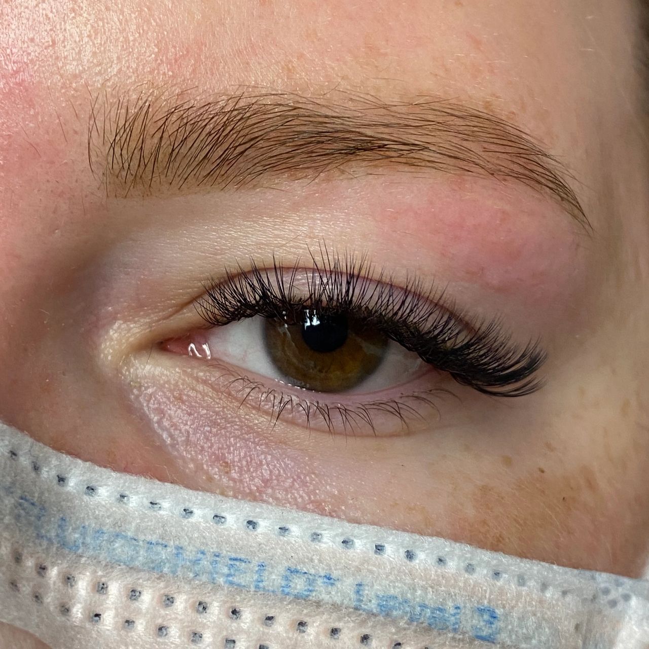Close-up of a brown eye with voluminous eyelash extensions and a white eye patch underneath.