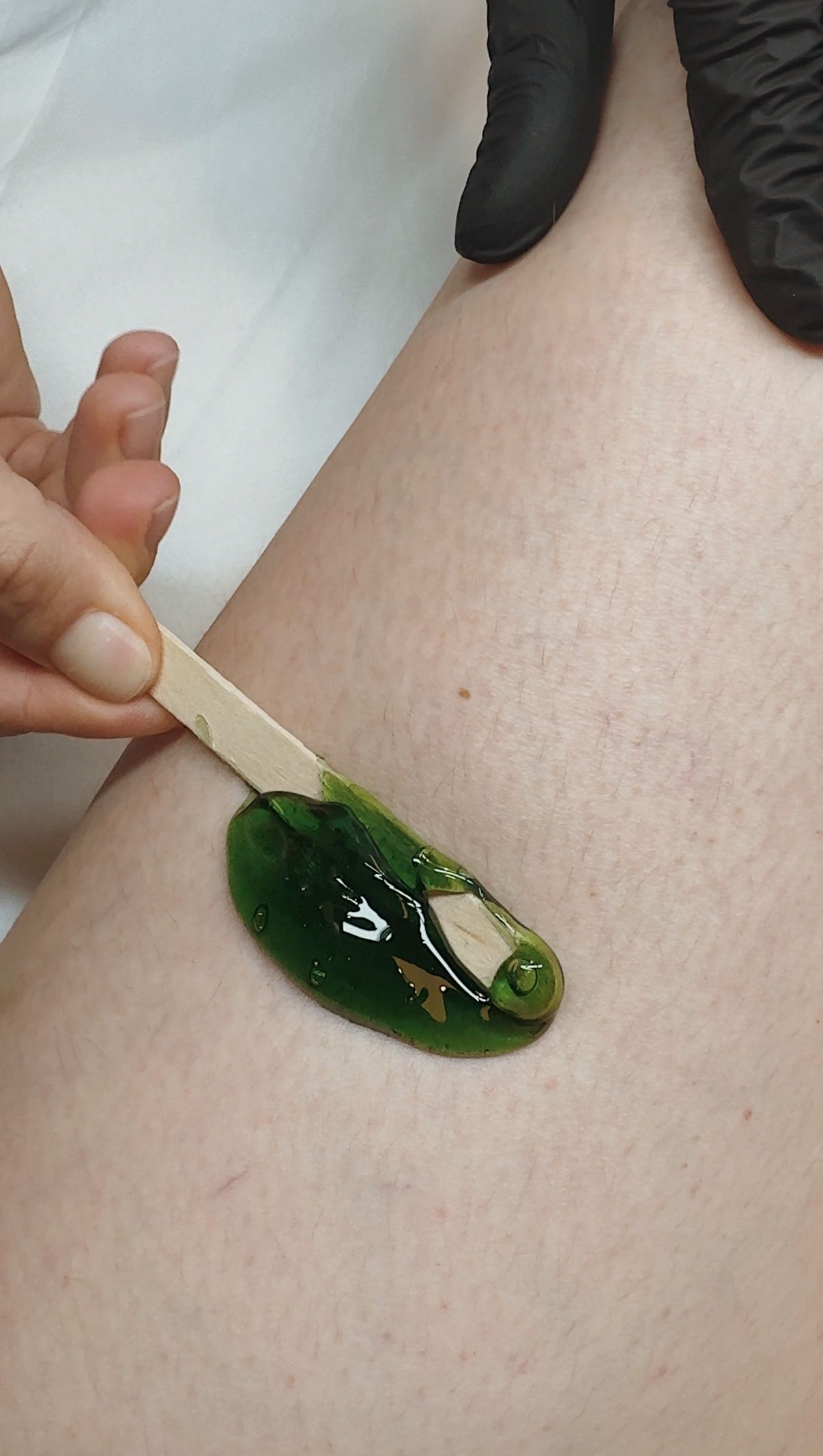 a hand applies green wax on a spatula to a leg