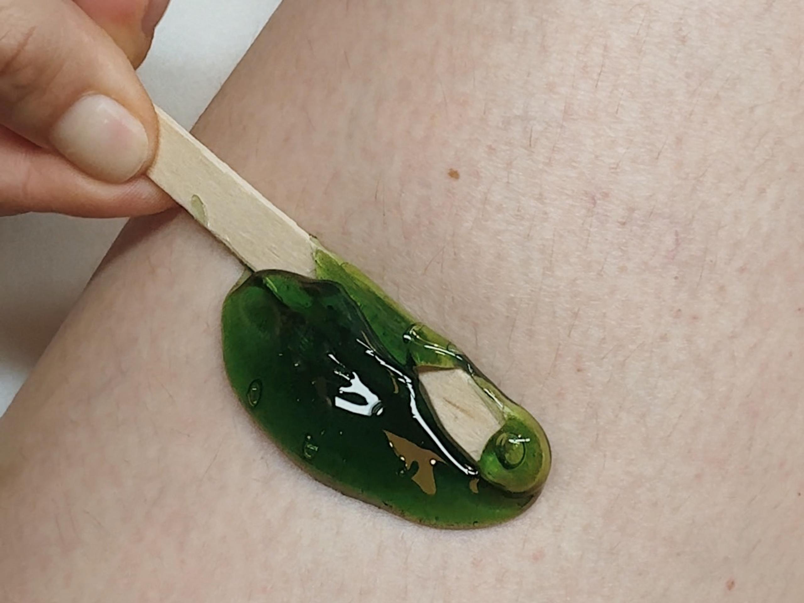 a hand applies green wax on a spatula to a leg