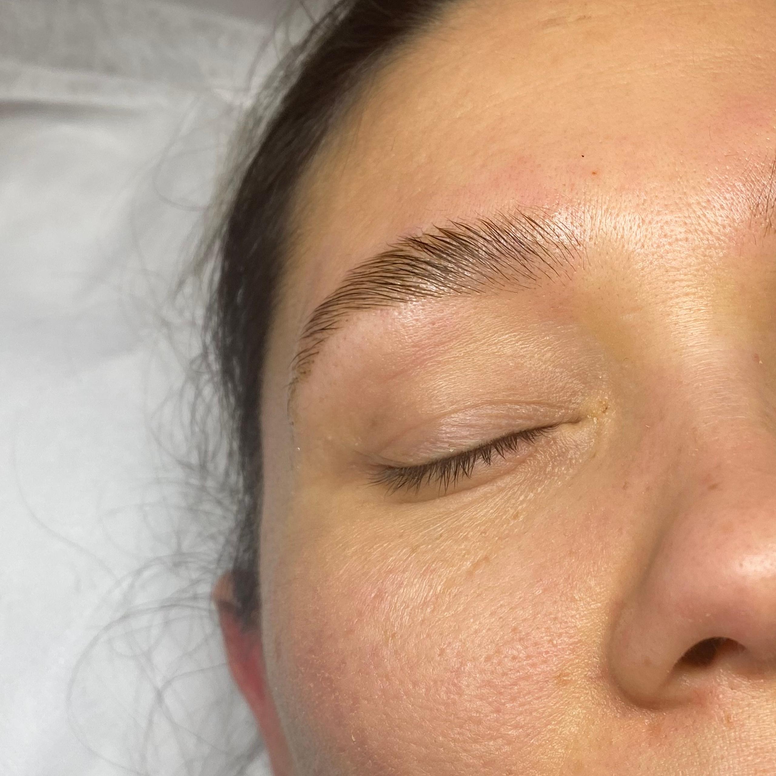 A woman's face with closed eyes, showing freshly laminated eyebrows with slight redness.