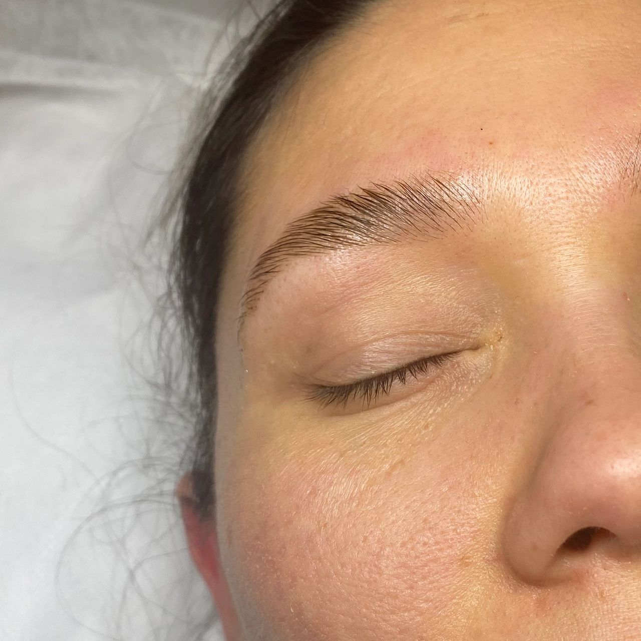 A woman's face with closed eyes, showing freshly laminated eyebrows with slight redness.