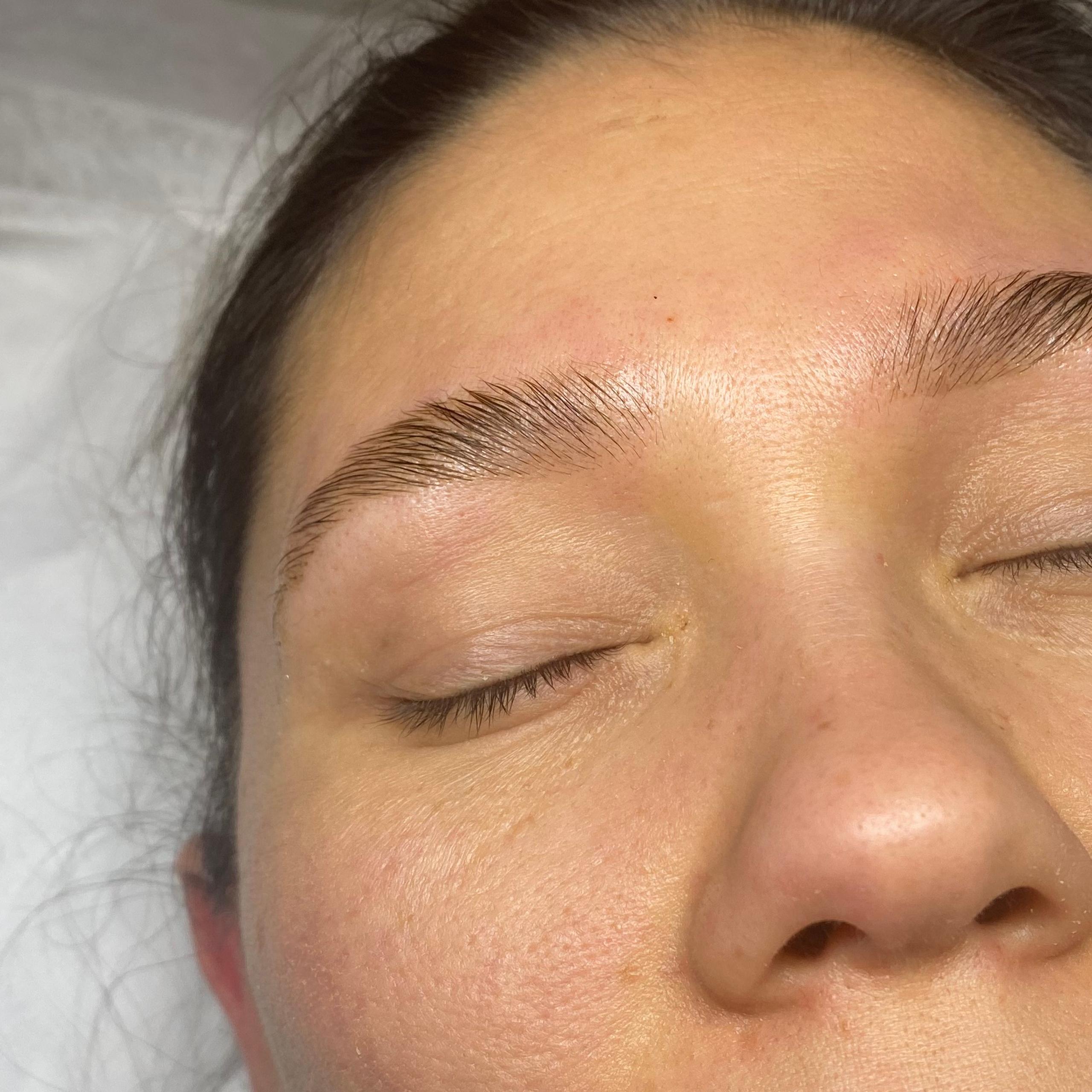 A woman's face with closed eyes, showing freshly laminated eyebrows with slight redness.